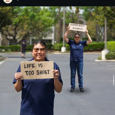 Two people holding signs, one reading Life is too short